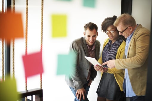 Three coworkers looking at iPad, colorful post-it notes in foreground